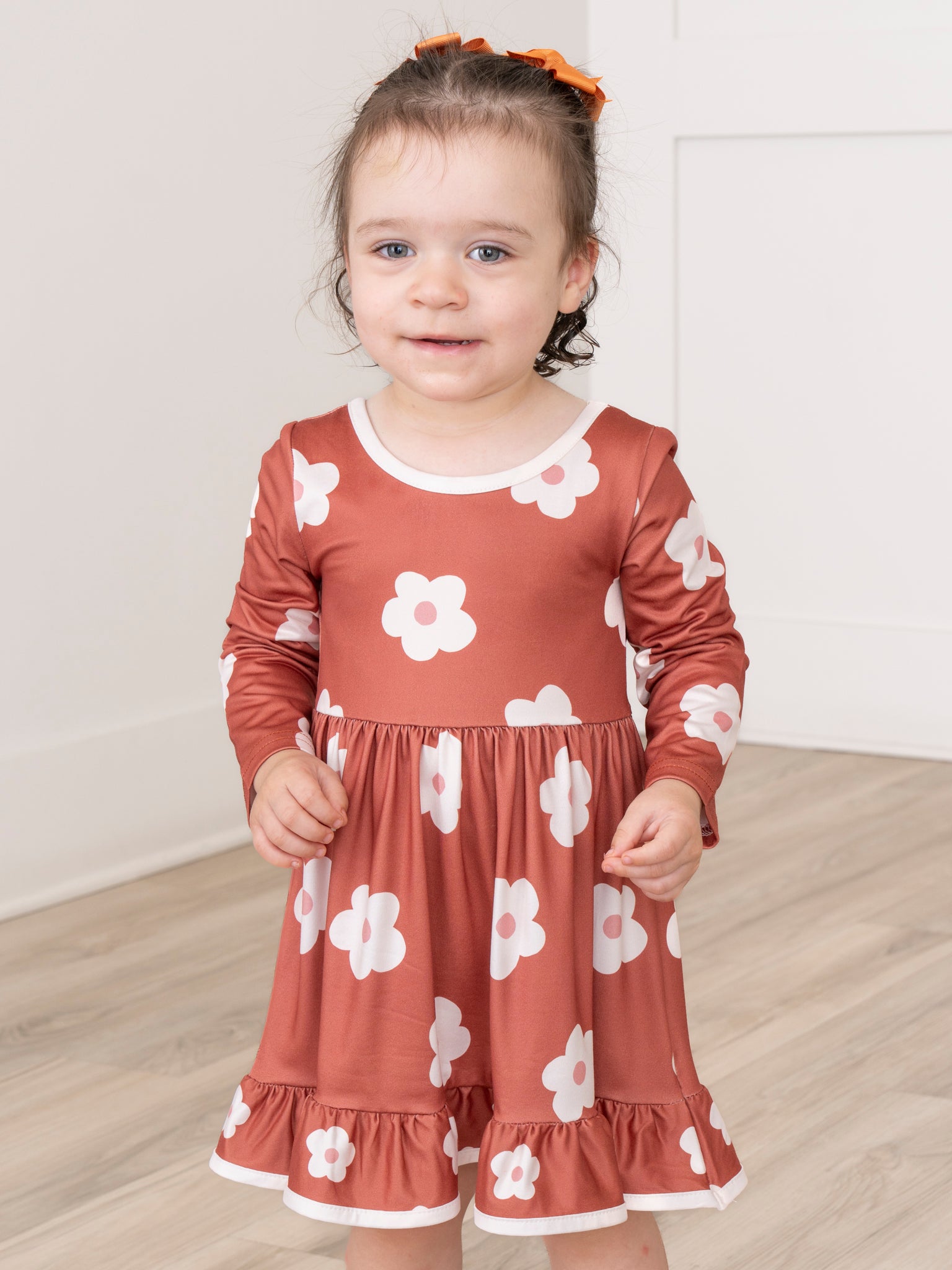 Child wearing a red dress with white floral patterns on a wooden floor.