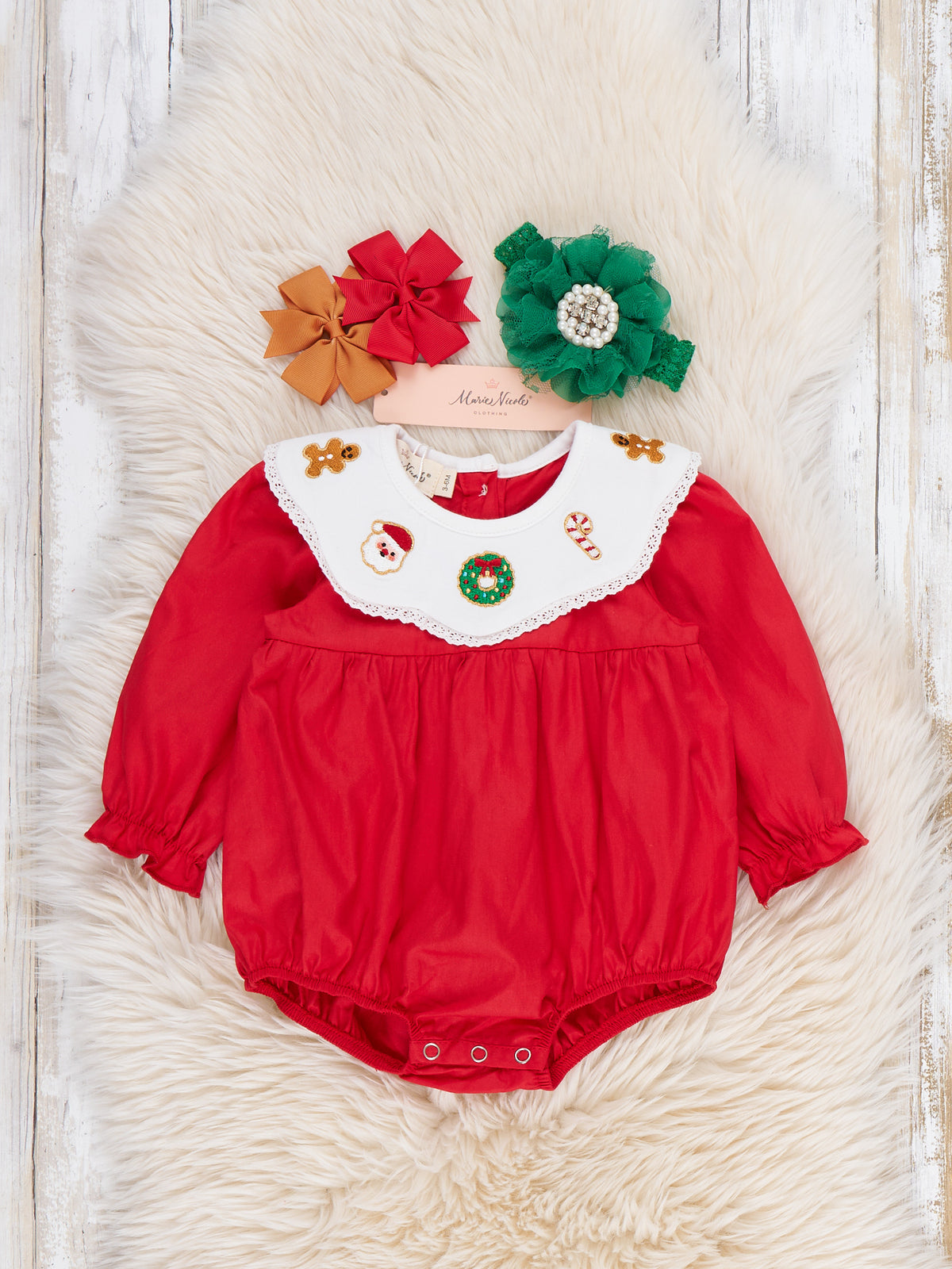 A baby red long-sleeve romper with a white ruffled collar decorated with holiday motifs, displayed on a white faux fur rug with three matching flower headbands.