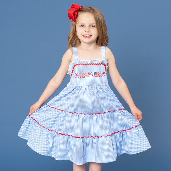 young girl wears patriotic gingham dress in front of blue background